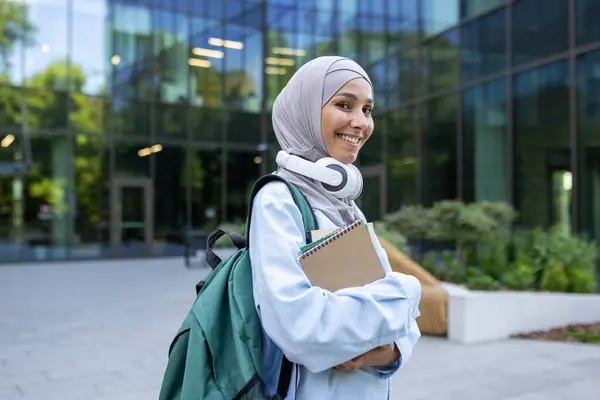 A contemporary student carrying a backpack and books walks in front of a glass building, exuding confidence and purpose.