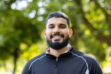 Yeşilliklerin arasında dikilmiş, yemyeşil bir parkın dinginliğini ve sakinliğini yaşayan, günlük kıyafetli bir adamın arka görüntüsü..