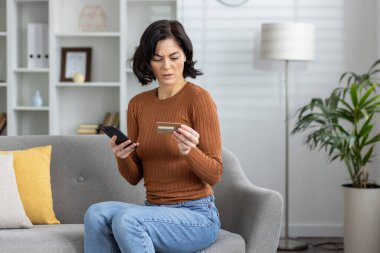 Akıllı telefon ve kredi kartı kullanan alarmlı bir kadın, çevrimiçi işlem sırasında bir dolandırıcılık hatasıyla karşı karşıya..