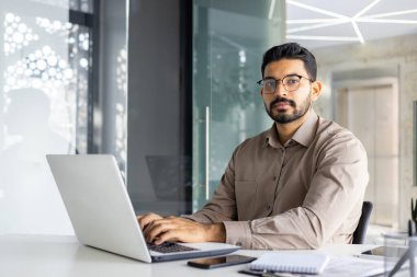 Modern bir ofiste özenle çalışan Hintli profesyonel bir işadamı özgüven ve adanmışlığı tasvir ediyor..