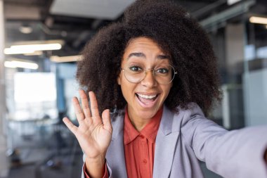 Afro-Amerikalı bir kadının modern akıllı telefondan ofis içi kamerayla çevrimiçi görüntüsünü ilk alan kişi. Orta kıvırcık saçlı çekici bir kadın sohbet sırasında el sallıyor..