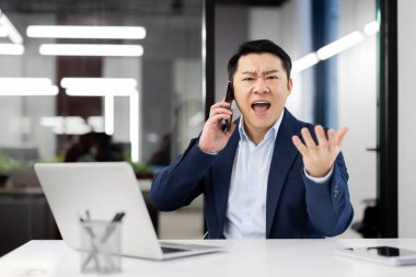 Sinirli Çinli adam çığlık atarken arka plandaki cam ofis duvarında telsiz akıllı telefondan konuşuyor. Kötü iş adamı, meslektaşlarıyla iletişim kurmak için modern aletler kullanıyor..