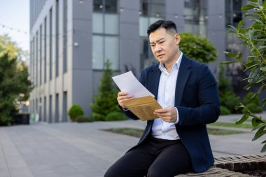 Üzgün genç bir ofis çalışanı, dışarıda bir bankta oturuyor ve aldığı mektup ile belgeyi okuyor..