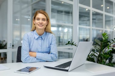 İş yerinde laptopla, tabletle ve modern ofis ortamında kapalı alanda gülümseyen kendine güvenen bir kadın profesyonel..