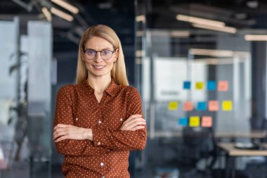 Günümüz ofis ortamında kolları çapraz duran, kendine güvenen bir iş kadınının portresi profesyonellik ve pozitiflik yayıyor..