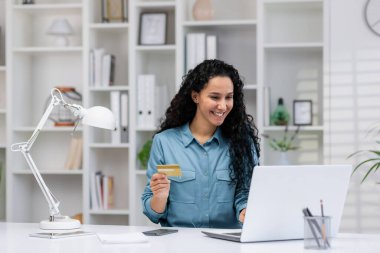 Gülümseyen İspanyol kadın rahat ofisinden online işlemler yapıyor, uzaktan çalışmalar ve finansal yönetim sergiliyor..