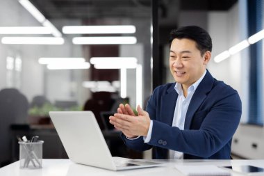 Modern ofis ortamında iş arkadaşlarıyla çevrimiçi bir video görüşmesine katılan profesyonel işadamı el çırpıyor.