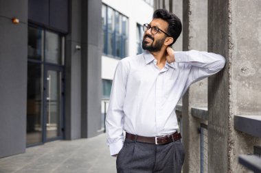 Yorgun Hintli genç bir ofis çalışanı binanın dışında el ele tutuşup masaj yapıyor ve gergin hissediyor. Acıdan buruşmuş.