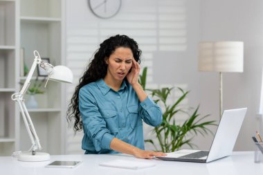 A distressed Hispanic woman is holding her ear in pain while working at her home office. She looks concerned and uncomfortable. clipart