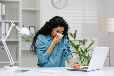 Ofis masasında çalışırken mendil kullanan genç bir iş kadını soğuk algınlığı belirtileri gösteriyor..