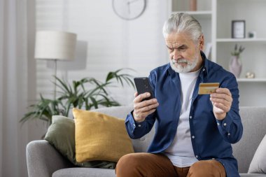 Evde bir kanepede oturan, akıllı telefonunu kullanan ve elinde kredi kartı tutan, muhtemelen online ödeme yapan ya da internetten alışveriş yapan son sınıf öğrencisi..