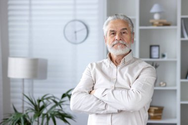 Kollarını kavuşturmuş kendinden emin bir adamın portresi şık döşeli bir evde duruyor memnuniyet ve olgunluk gösteriyor..