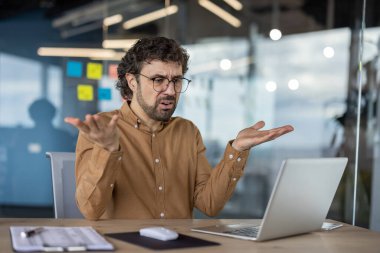Güncel ofis ortamında dizüstü bilgisayar kullanan, sıradan iş yeri sorunlarını yansıtan, günlük gömlekli yetişkin bir erkek kafa karışıklığı gösterir..