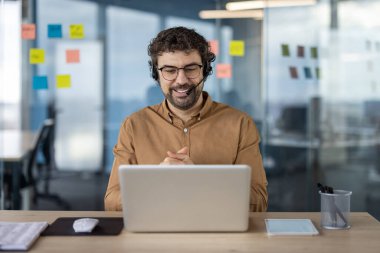 Modern bir ofis ortamında iş görüşmesinde kulaklık takan gülümseyen İspanyol işadamı. Profesyonel, nişanlı ve odaklanmış..