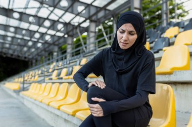 Stadyumun merdivenlerinde otururken dizini ağrıyan bir kadın, sporla ilgili bir diz sakatlığı olduğunu gösteriyor..