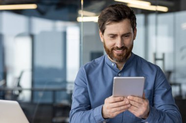 Çağdaş bir ofis içinde, bir tablet üzerinde gülümseyen iş dünyası profesyoneli gezinmesi, bağlantı ve teknolojiyi sembolize eder..