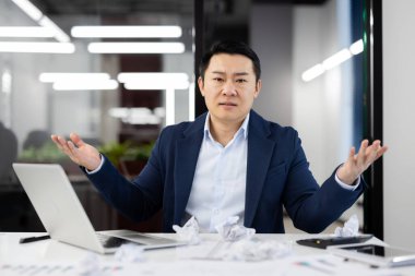 Buruşuk kağıtlar ve bilgisayarlarla dolu bir masada otururken ciddi bir ofis yöneticisi kollarını kaldırıyor. Yoğun erkek, tatilden sonra ofise dönerken iş ile boğuşuyor..