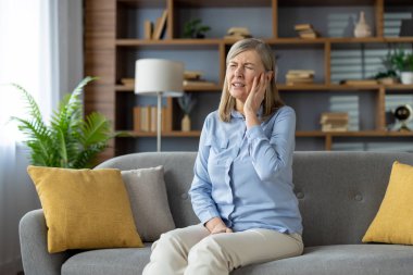 Sıkıntılı insan gri koltukta oturur ve ağız hastalığına yakalanırken avuçlarını avuçlar. Dişe duyarlılık hastalığından muzdarip yaşlı bir kadın ve dişlerle ilgili dayanılmaz problemler..