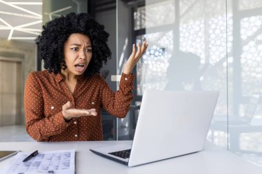 Bir Afrikalı Amerikalı iş kadını, modern ofis ortamında bilgisayarına öfke ve hüsran göstererek işyeri stresini ifade ediyor..