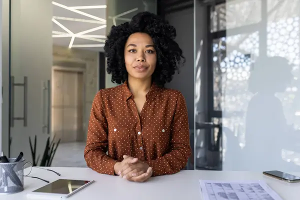 一位穿着时髦的波尔卡圆点衬衫的自信的年轻非洲裔美国女人在她的工作空间摆设着一个平板电脑和一个蓝图 在一个明亮的现代办公环境中 — 图库照片