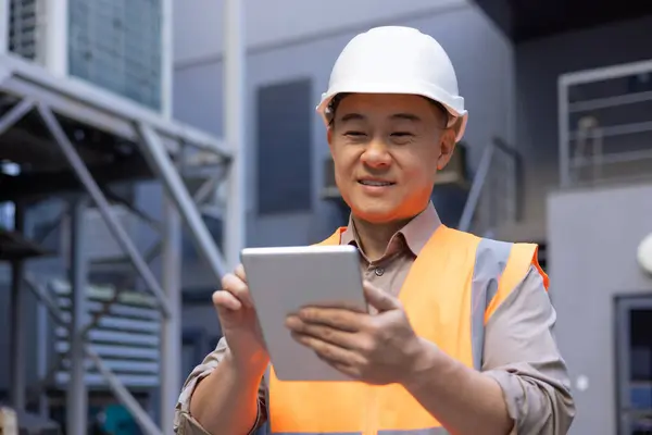 A smiling Asian man is working on a construction site. foreman, foreman. Standing outside and using a tablet. Close-up photo.