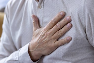 Bu görüntü, orta yaşlı bir adamın kalp atışlarını hissedişinin yakın plan görüntüsünü yakalıyor. Eline ve gömleğinin dokusuna odaklanarak sağlığını ve sağlığını gösteriyor..