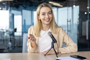 Canlı bir görüntülü sohbet sırasında mikrofona konuşan kendinden emin profesyonel bir kadın. Bağlı ve dost canlısı, modern ofis ortamında etkili bir şekilde iletişim kuruyor..