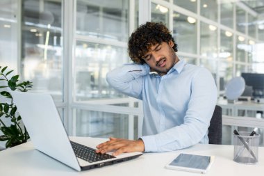 Masaüstünde gözlerini kısarak otururken boynunu ovuşturup başını eğen Latin bir adamla boğuşuyor. Omurilik sorunu ve ofis sendromu belirtileri gösterirken sağlıksız adam masaj yapıyor..