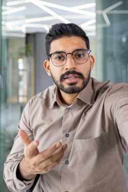 Pamuklu gömlekli esmer adamın şık gözlükler taktığı ve video toplantısı sırasında kameraya el kol hareketi yaptığı ilk kişi. Arap şirketinin patronu önemli bilgileri bölüm işverenleriyle paylaşıyor..