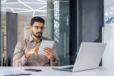 Bilgisayarla birlikte masaüstü sandalyeye yaslanırken, dizüstü bilgisayarda Latin kökenli serbest yazar kontrol listesi. Ofisin içinde şık bir şekilde otururken günlüğe yazılmış genç profesyonel yorumlar..