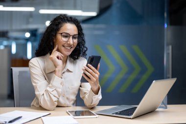 Ofisteki güzel kadın, mutlu ve gülümseyen Latin Amerikalı iş kadını internet telefonunu kapatıyor, kadın çalışan mesajları okuyor ve ofis içi internet sayfalarını karıştırıyor..