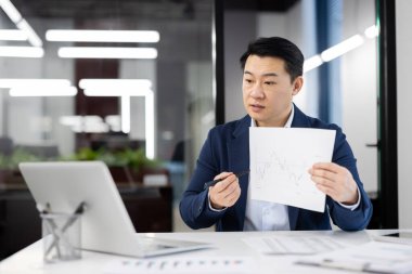 İyi ışıklandırılmış, çağdaş bir ofis ortamında video konferans düzenlerken kendine güvenen Asyalı işadamı finansal bir tablo sunuyor. Kurumsal analitik ve pazar eğilimlerini resmediyor.