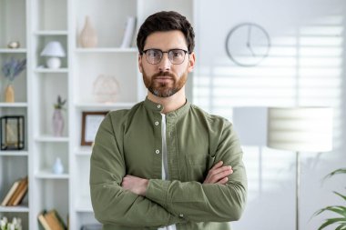 Profesyonel bir adam, çağdaş, aydınlık bir ofis ortamında, liderlik ve uzmanlık yayarak çapraz kollarla güven içinde poz verir..