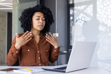 Genç bir Afrikalı Amerikalı kadın şık, güneşli bir ofiste tek başına çalışırken rahatsız ve terli görünüyor. Sıcaklık hissediyor..