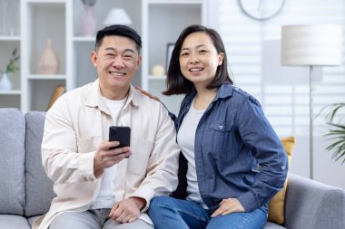 Neşeli orta yaşlı bir çift oturma odasındaki kanepede rahat bir anın tadını çıkarıyor. Adamın elinde akıllı bir telefon var, ikisi de içten gülümsüyor. Sıradan giyinmişler.