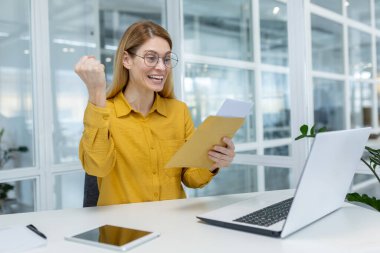 Sarı bluzlu neşeli genç iş kadını başarılı bir haberi ya da parlak bir ofis ortamında kontratı kutluyor..