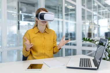 Parlak bir ofis ortamından sanal bir toplantıya katılmak için VR kulaklığı kullanan genç bir bayan profesyonel nişanlı..