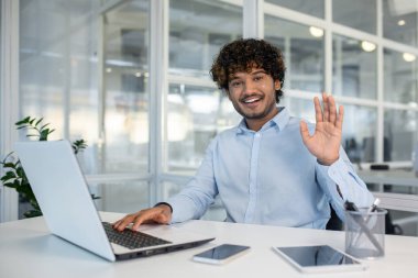 Modern ofis ortamında çevrimiçi bir toplantı sırasında dizüstü bilgisayara el sallayan gülümseyen iş adamı. Uzaktan çalışma ve iletişimi gösteren sanal bir konferans görüşmesine bağlandı..