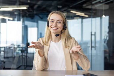 Modern ofis ortamında masada otururken kulaklık takan gülümseyen müşteri hizmetleri temsilcisi..