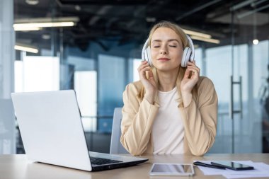 Dingin bir görüntü, kulaklıklı sarışın bir iş kadınını müzik dinlerken, gözleri kapalı, çalışma odasında modern bir ofis ortamında yakalıyor..
