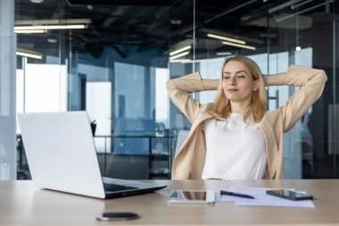 Profesyonel bir kadın iş yerinde rahatça esneyerek mola verir. Modern bir ofis alanı üretkenlik ve rahatlama için mükemmel bir zemin görevi görür..