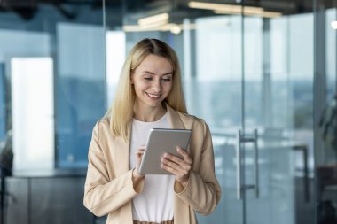 Parlak, çağdaş bir ofis ortamında dijital tabletle meşgul olan genç profesyonel bir kadın. İş kıyafetlerine güven ve verimlilik yayıyor..