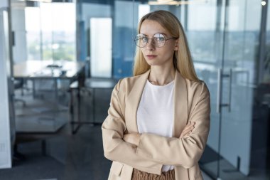 Kendine güvenen iş kadını modern ofis ortamında çapraz duruyor, liderlik, profesyonellik ve kararlılık gösteriyor..