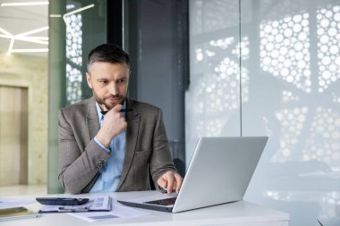 Modern ofis masasında özenle dizüstü bilgisayar üzerinde çalışan bir işadamı, konsantrasyonu olan bir projeye odaklanıyor..