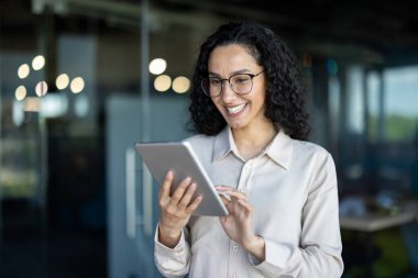 Çağdaş bir ofis ortamında dijital tablet kullanan gülümseyen iş kadını, çalışma aktiviteleriyle meşgul.