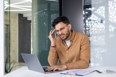 Ofis masasında evrak ve tabletle çalışırken kafası ağrıyan bir adam..