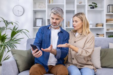Olgun çift, modern oturma odalarında rahat bir kanepede otururken akıllı telefon sorunları hakkında ciddi bir konuşma yapıyorlar..