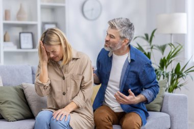 Orta yaşlı bir çift oturma odalarında tartışırken görülüyor, evcil bir ortamda hayal kırıklığı ve üzüntü duygularını resmediyorlar..