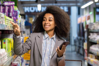 In a grocery store, a woman with curly hair and a formal jacket shops using a smartphone, pointing at products on a shelf, showcasing modern shopping habits and technology use in retail clipart