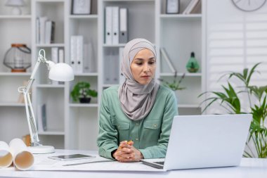 Başörtüsü tasarımcısı kadın, ev ofisinde çalışıyor, mimar işte dizüstü bilgisayar kullanıyor, online teknik ödev okuyor, ciddi ve konsantre okuma yapıyor..